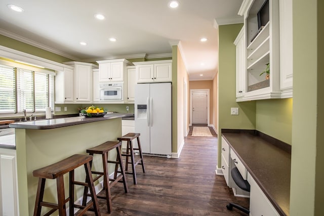 kitchen featuring white cabinets, white appliances, dark hardwood / wood-style floors, a kitchen breakfast bar, and ornamental molding