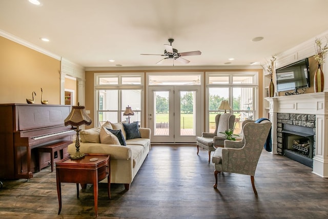 living room featuring crown molding, ceiling fan, dark hardwood / wood-style floors, and a stone fireplace