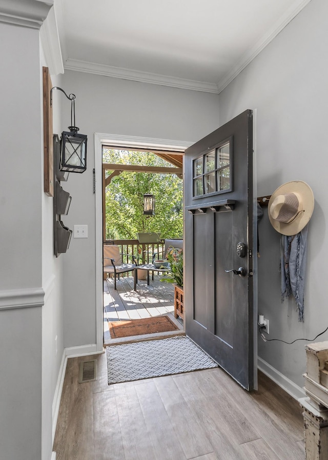entryway with baseboards, wood finished floors, visible vents, and ornamental molding