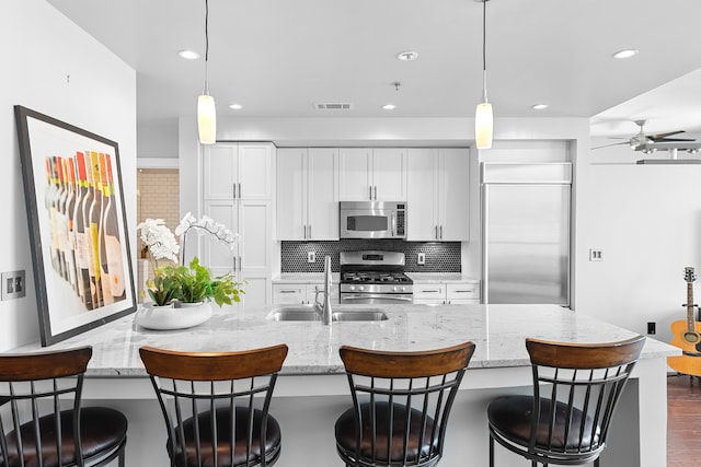 kitchen with appliances with stainless steel finishes, a breakfast bar area, light stone countertops, and ceiling fan