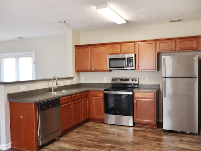 kitchen featuring a textured ceiling, dark hardwood / wood-style floors, stainless steel appliances, sink, and kitchen peninsula