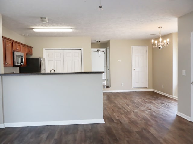 kitchen with pendant lighting, ceiling fan with notable chandelier, a textured ceiling, dark hardwood / wood-style flooring, and appliances with stainless steel finishes