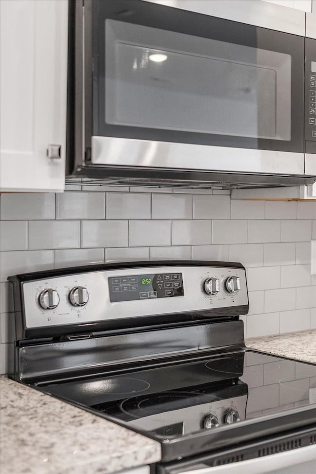 interior details featuring light stone countertops, white cabinetry, appliances with stainless steel finishes, and backsplash