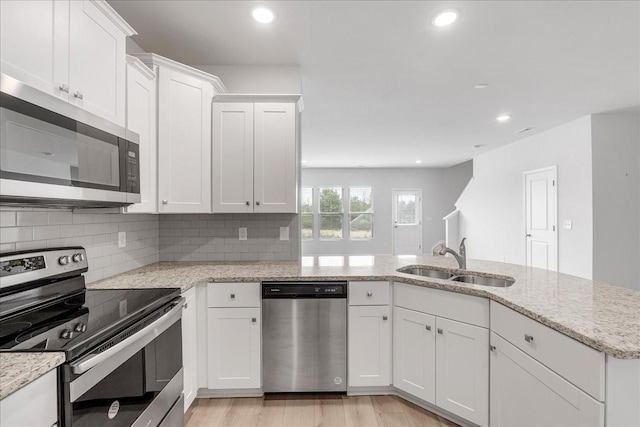 kitchen with stainless steel appliances, a sink, white cabinets, backsplash, and light wood finished floors