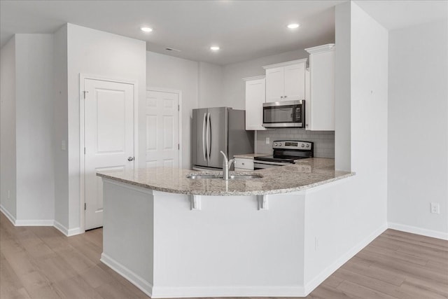 kitchen featuring tasteful backsplash, appliances with stainless steel finishes, light stone counters, light wood-style floors, and a sink