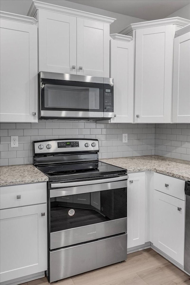 kitchen featuring tasteful backsplash, white cabinets, appliances with stainless steel finishes, light stone counters, and light wood-type flooring