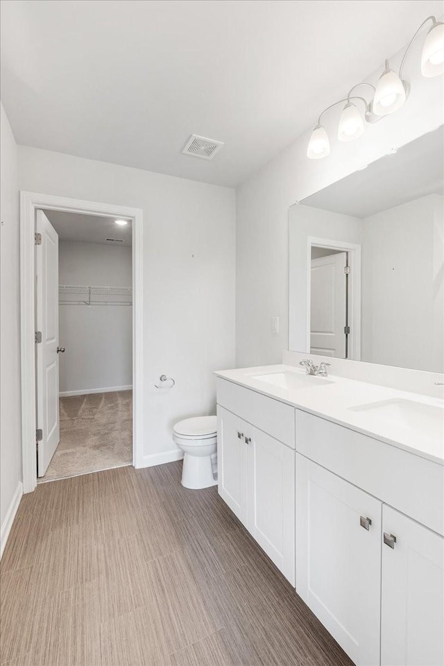 bathroom featuring toilet, double vanity, visible vents, and a sink