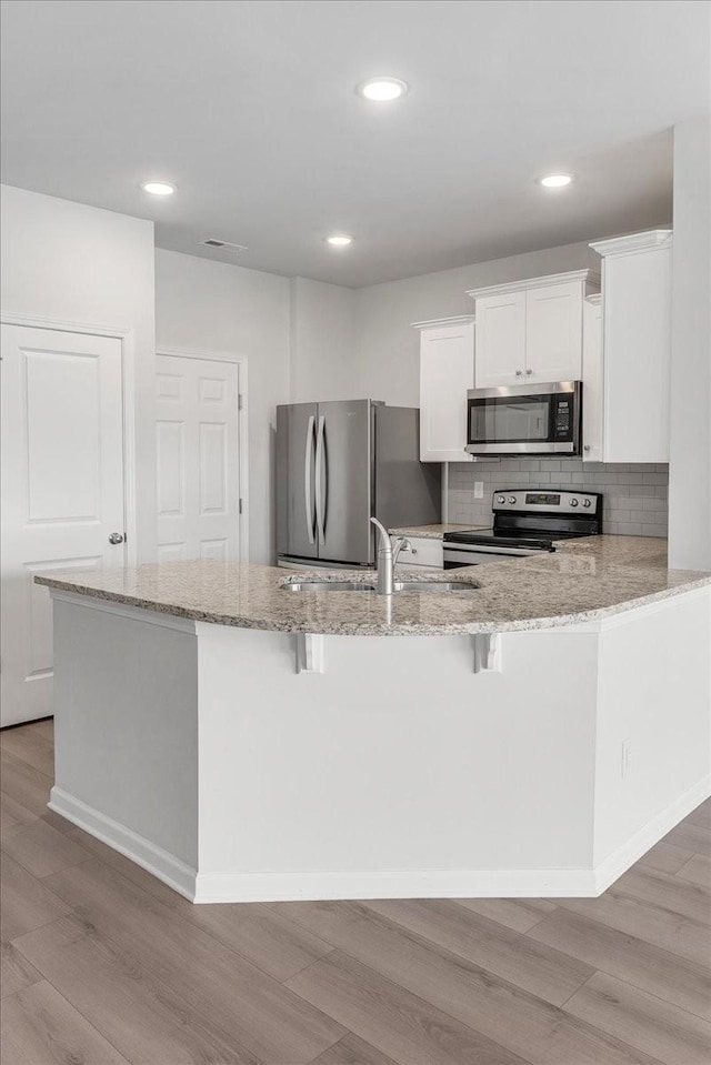 kitchen with light wood-style floors, appliances with stainless steel finishes, and light stone counters