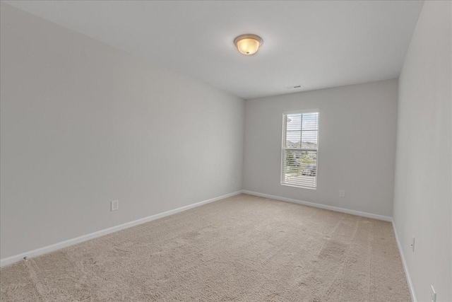 spare room featuring light colored carpet and baseboards