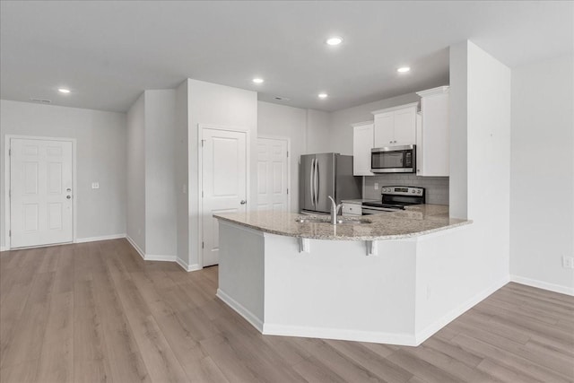 kitchen featuring light stone counters, stainless steel appliances, a peninsula, light wood-type flooring, and decorative backsplash