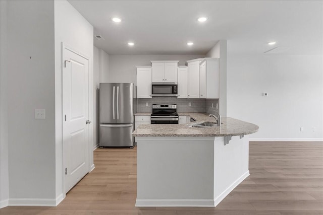 kitchen with stainless steel appliances, a peninsula, a sink, light wood-type flooring, and light stone countertops