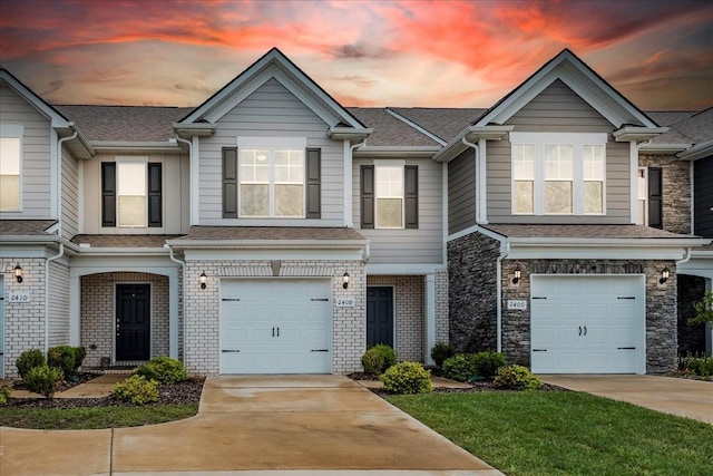 multi unit property featuring brick siding, roof with shingles, concrete driveway, an attached garage, and stone siding