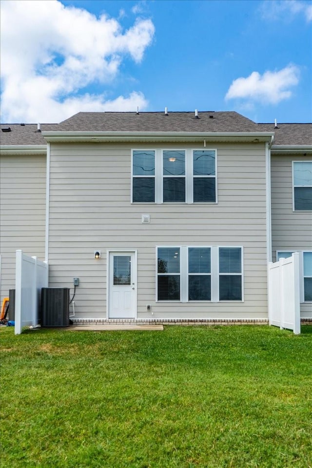 rear view of property featuring fence, a lawn, and central AC