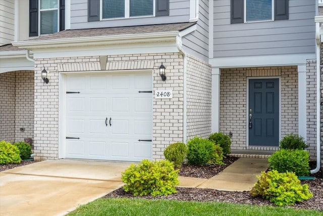 doorway to property featuring a garage, driveway, and roof with shingles