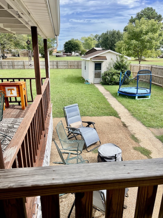 wooden deck featuring a trampoline, a storage shed, and a yard