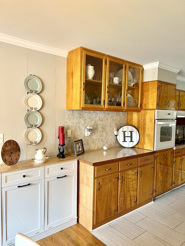 kitchen with ornamental molding, white oven, decorative backsplash, and light hardwood / wood-style floors