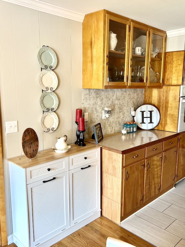 bar featuring light wood-type flooring, crown molding, oven, and decorative backsplash