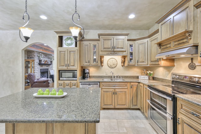 kitchen with a fireplace, stone countertops, appliances with stainless steel finishes, a center island, and sink