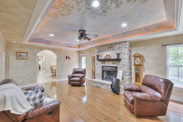 living room with a fireplace, a raised ceiling, ceiling fan, and light hardwood / wood-style floors