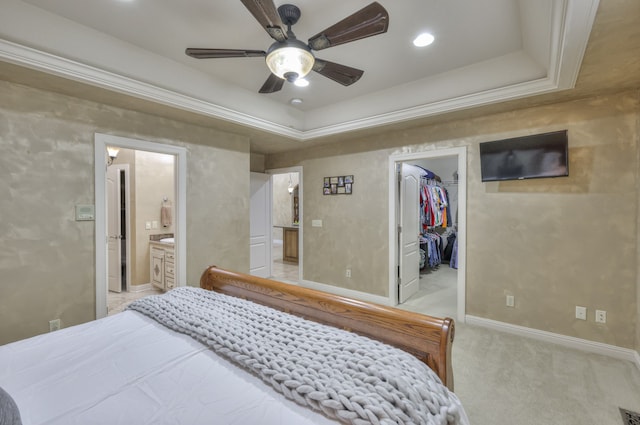 bedroom with ensuite bath, a closet, a tray ceiling, a spacious closet, and ceiling fan