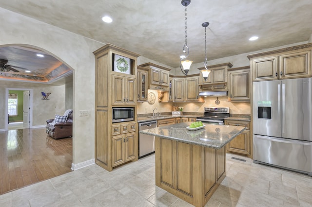 kitchen featuring dark stone countertops, light wood-type flooring, appliances with stainless steel finishes, ceiling fan, and a kitchen island