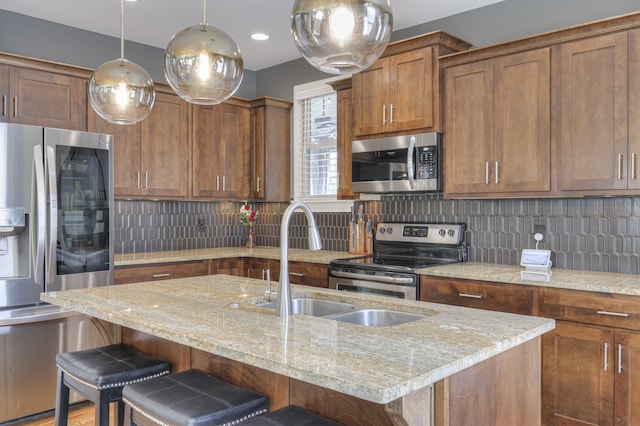 kitchen with decorative light fixtures, light stone counters, stainless steel appliances, a kitchen breakfast bar, and a kitchen island with sink