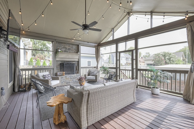 sunroom with lofted ceiling, ceiling fan, and a stone fireplace