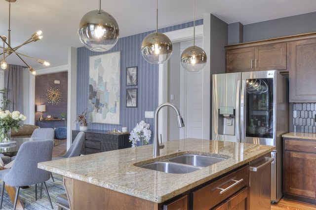 kitchen featuring light stone countertops, a center island with sink, pendant lighting, sink, and a chandelier