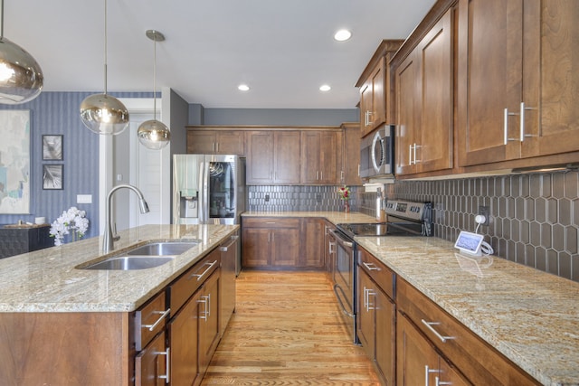 kitchen featuring pendant lighting, light hardwood / wood-style flooring, an island with sink, sink, and appliances with stainless steel finishes