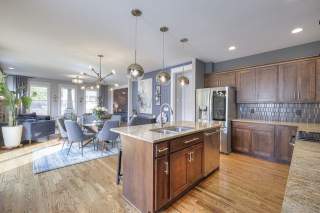 kitchen featuring light wood-type flooring, light stone counters, stainless steel appliances, and sink