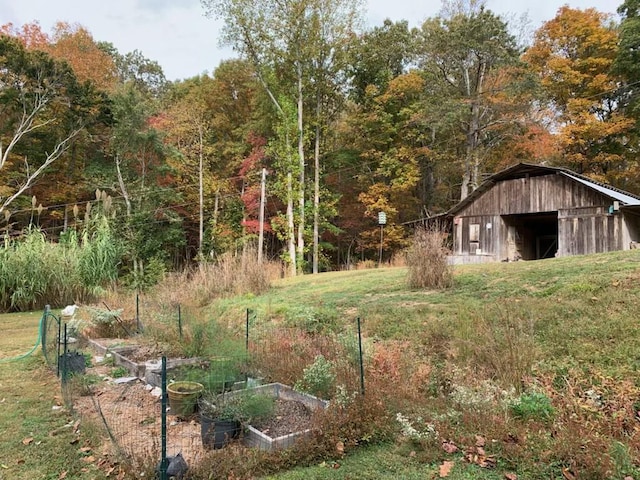 view of yard featuring an outbuilding, a barn, a vegetable garden, and a view of trees