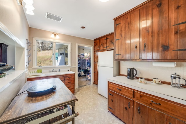 kitchen with brown cabinets, visible vents, light countertops, and freestanding refrigerator