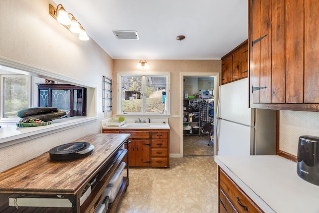 kitchen with a sink, visible vents, light countertops, freestanding refrigerator, and brown cabinets