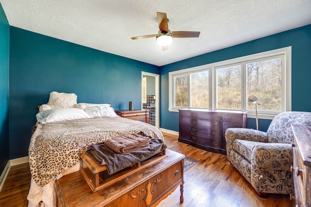 bedroom with a ceiling fan, a textured ceiling, baseboards, and wood finished floors