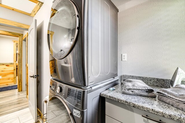 clothes washing area with light hardwood / wood-style flooring and stacked washer / drying machine