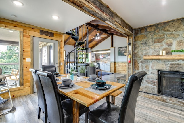 dining area featuring a fireplace, lofted ceiling with beams, wood walls, and light hardwood / wood-style floors