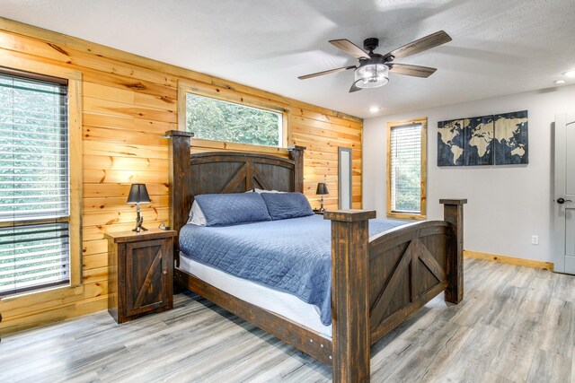 bedroom featuring light hardwood / wood-style flooring, ceiling fan, wooden walls, and multiple windows