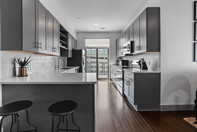 kitchen featuring gray cabinets, backsplash, dark hardwood / wood-style flooring, kitchen peninsula, and appliances with stainless steel finishes