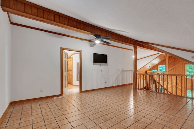 unfurnished living room with light tile patterned floors, vaulted ceiling, wood walls, ceiling fan, and a textured ceiling