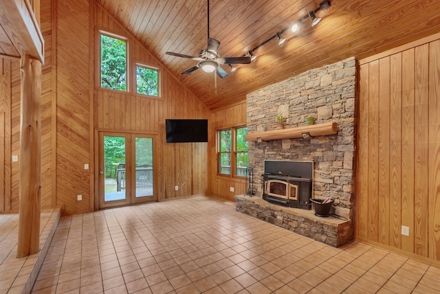 unfurnished living room with track lighting, a wood stove, wood walls, and ceiling fan