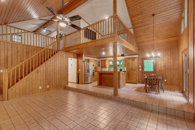 unfurnished living room featuring high vaulted ceiling, wood walls, ceiling fan with notable chandelier, and tile patterned flooring