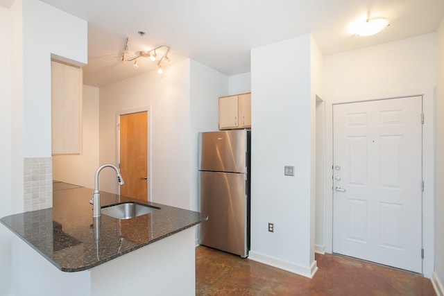 kitchen with light brown cabinetry, sink, stainless steel fridge, dark stone counters, and kitchen peninsula