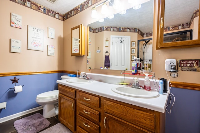 full bathroom with double vanity, toilet, a textured ceiling, and a sink