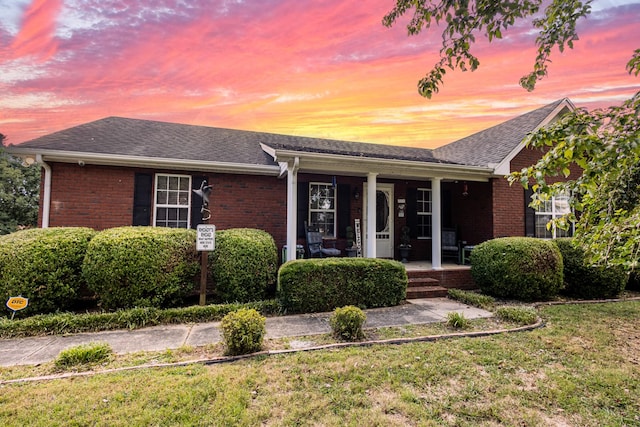 ranch-style home featuring brick siding, a yard, a porch, and roof with shingles