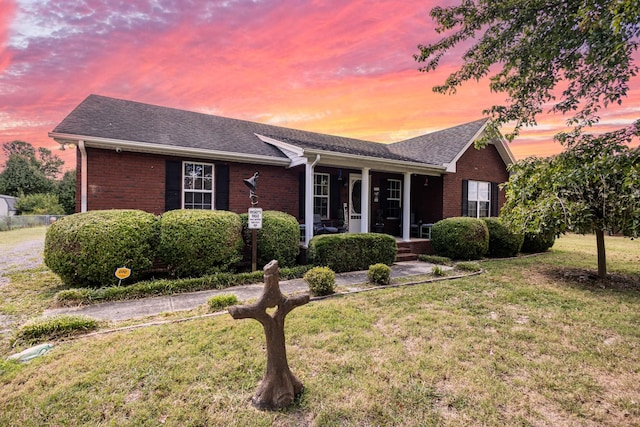 single story home with brick siding, a porch, a shingled roof, and a yard