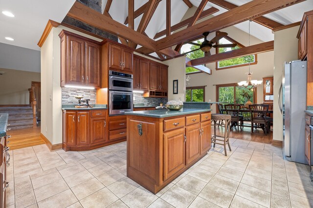 kitchen with backsplash, high vaulted ceiling, stainless steel appliances, ceiling fan with notable chandelier, and a center island