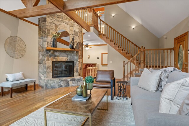 living room featuring ceiling fan, high vaulted ceiling, a stone fireplace, and hardwood / wood-style floors