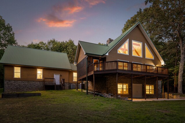 back house at dusk featuring a wooden deck, a patio area, and a lawn