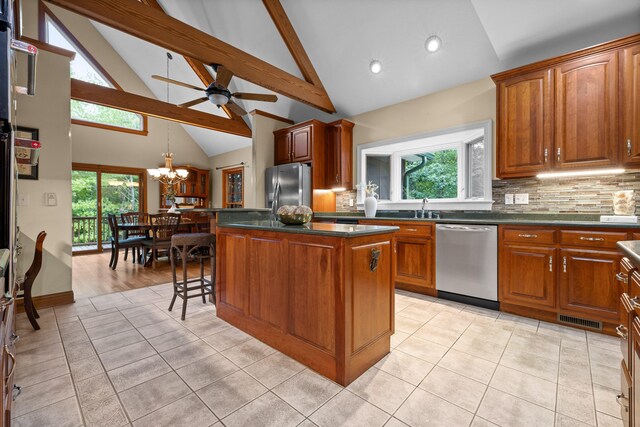 kitchen with ceiling fan with notable chandelier, a kitchen island, stainless steel appliances, high vaulted ceiling, and decorative backsplash