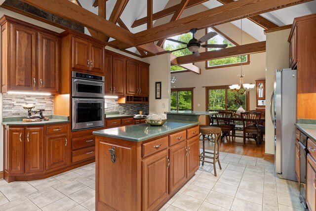 kitchen with ceiling fan with notable chandelier, a healthy amount of sunlight, decorative backsplash, and a kitchen island